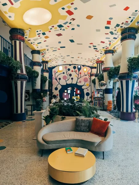 Farbenfrohe Hotellobby mit Couch, Pflanzen und bemalter Decke