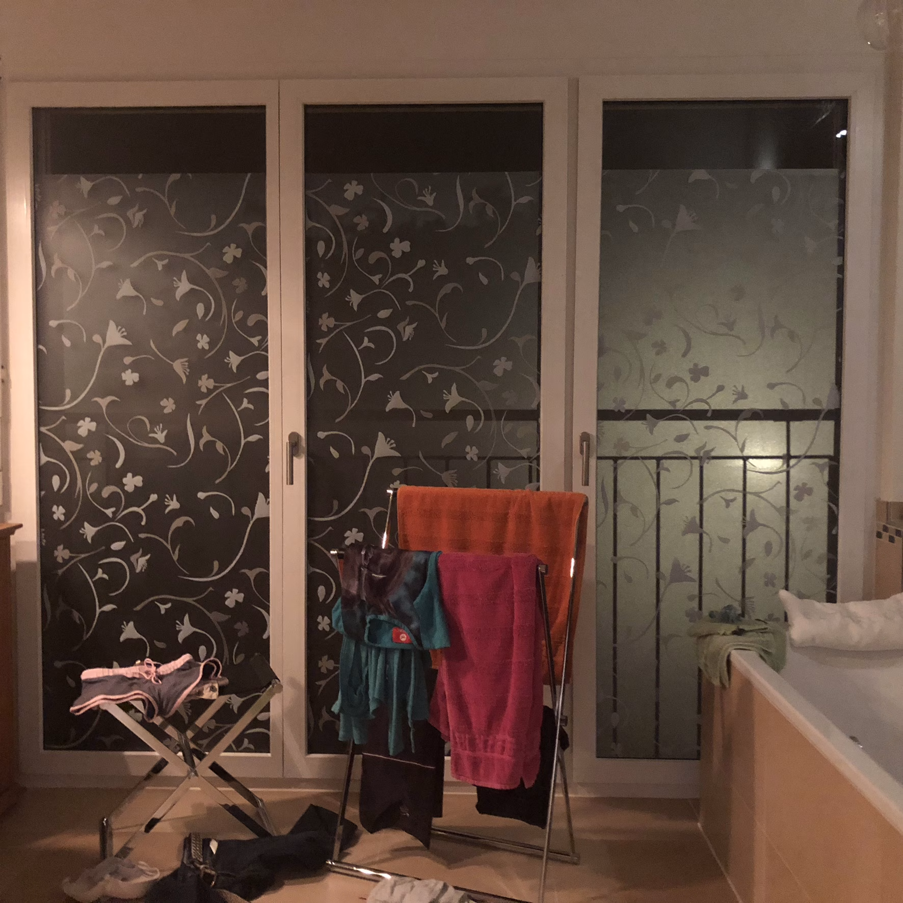 Kleberlose Folie matt mit weißen Blumen auf einem Badezimmerfenster angebracht in Innenansicht bei Nacht.