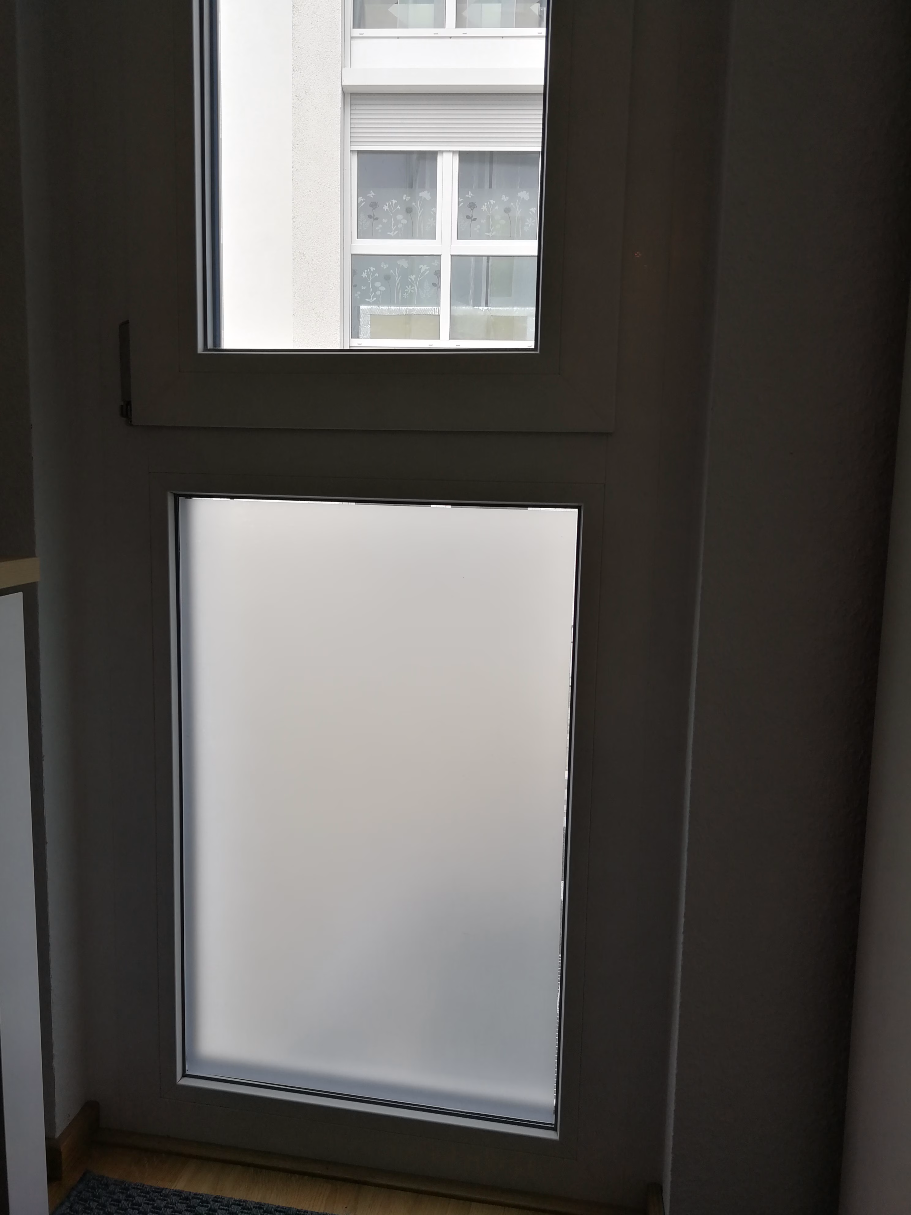 Eine weiß matte, selbsthaftende Sichtschutzfolie auf einem feststehenden Fenster angebracht