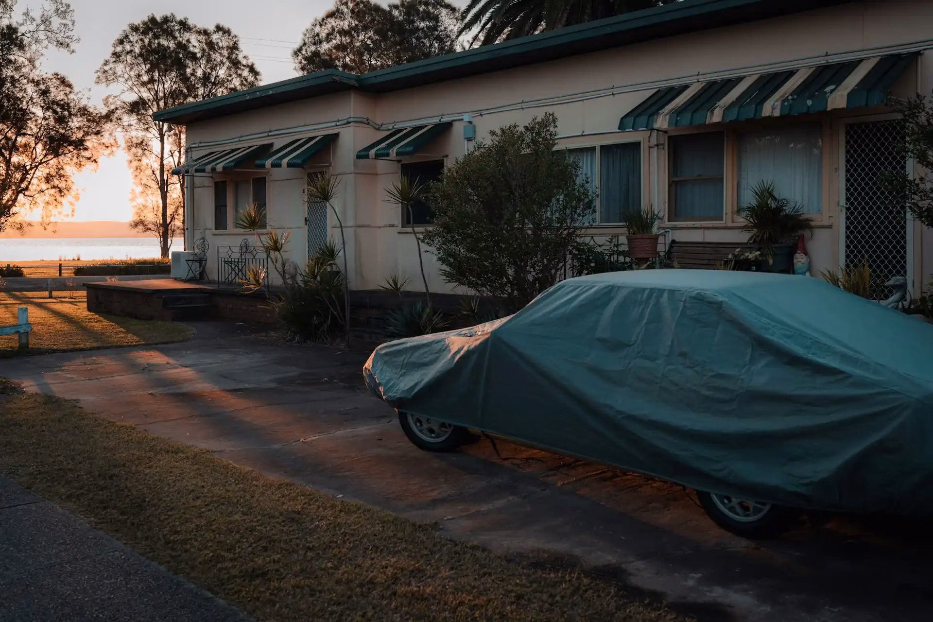 Auto mit Schutzabdeckung vor einem Haus bei Sonnenuntergang